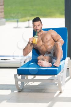 Young Man Resting On Sun Loungers By Swimming Pool With Orange Juice