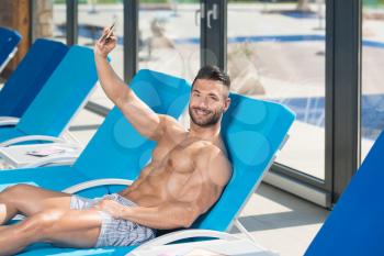 Young Man Resting On Sun Loungers By Swimming Pool and Making a Selfie With Phone