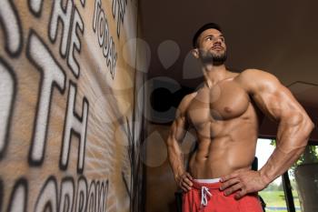 Portrait of a Young Physically Fit Man in White T-shirt Showing His Well Trained Body - Muscular Athletic Bodybuilder Fitness Model Posing After Exercises In Front Of A Graffiti Wall