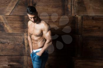 Portrait of a Young Physically Fit Man Showing His Well Trained Body While Wearing Blue Jeans - Muscular Athletic Bodybuilder Fitness Model Posing After Exercises on Wooden Wall - a Place for Your Text