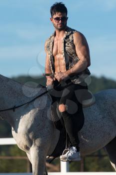 Handsome Macho Man Cowboy Riding on a Horse - Background of Sky and Mountains