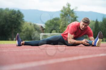 Sporty Man Stretching and Warming Up Legs for Running Fitness Workout on Track Exercising Outside