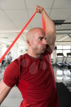 Attractive Man Exercising With A Resistance Band In Gym As Part Of Fitness Bodybuilding Training