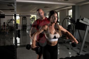 Young Couple Working Out In Gym - Doing Shoulders Exercise With Dumbbells