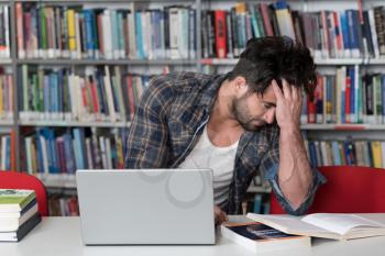 Stressed Young Male Student Reading Textbook While Sitting in Library