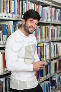 Portrait of a Happy Handsome Man Typing on Mobile Phone in Library at the University