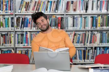 Handsome Man With Dark Hair Sitting at a Desk in the Library - Laptop and Organiser on the Table - Looking at the Screen a Concept of Studying - Blurred Books at the Back