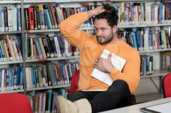 Stressed Young Male Student Reading Textbook While Sitting in Library