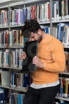 Male College Student Looks Tired While Studying With a Laptop and Textbooks in the Library