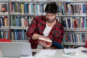 In the Library - Handsome Male Student With Laptop and Books Working in a High School - University Library - Shallow Depth of Field