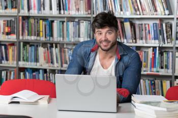 Handsome Male Student With Laptop and Books Working in a High School Library