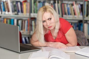 Stressed Young Female Student Reading Textbook While Sitting in Library