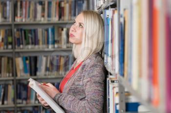 Pretty Woman With Blonde Hair Standing in the Library - Blurred Books at the Back