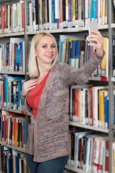 Beautiful Blonde Female College Student in Library and Taking Selfies With Mobile Phone