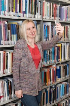 Portrait of a Happy Blonde Woman in Library at the University and Taking Selfies With Mobile Phone
