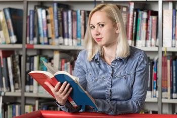 Pretty Woman With Blonde Hair Standing in the Library - Blurred Books at the Back