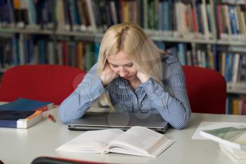 Stressed Young Female Student Reading Textbook While Sitting in Library