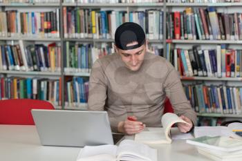 Man Student With Cap Working on Laptop and Books in a High School Library