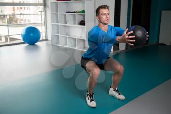 Handsome Young Man Doing Squad With Medicine Ball As Part Of Bodybuilding Training