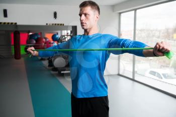 Attractive Man Exercising With A Resistance Band In Gym As Part Of Fitness Bodybuilding Training
