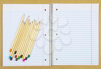 Multi-colored pencils on a blank notepad with a spiral