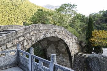Old arching bridge in China with mountains and sky in background