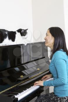Vertical photo of mature woman with her family cat on top of piano looking at each other while sitting at the piano