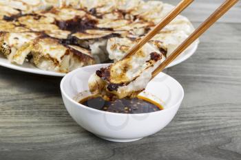 Freshly cooked Chinese dumplings with chopsticks, small white bowl and plate in background