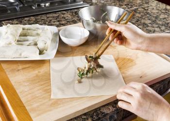 Female hands with wooden chopsticks putting fresh food ingredients on to spring roll wrap