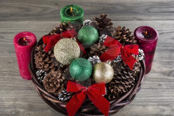 Seasonal holiday basket full of Christmas ornaments, ribbons and dried pine cones with lit candles in the background