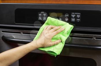 Hand with microfiber cleaning rag wiping outside of electric oven