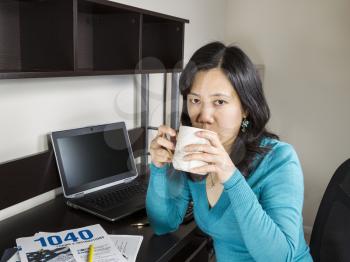 Mature Asian women drinking coffee with tax booklet and computer on desk