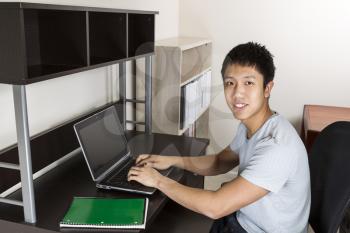 Young man studying at home office for college work with computer and notepad on desk