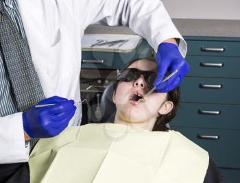 Horizontal photo of a male dentist preparing to examine young girl teeth with tools in tray in background