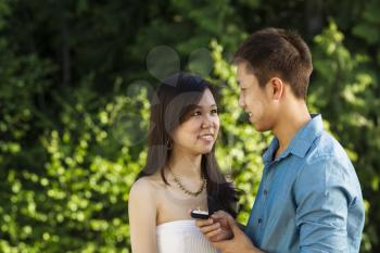 Horizontal photo of a young adult woman showing her happiness with the engagement ring presented by her boyfriend with blurred out green trees in background