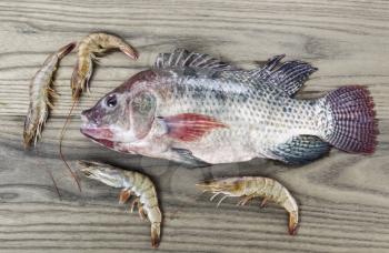 Freshly caught Tilapia fish with shrimp on aging ash wood background