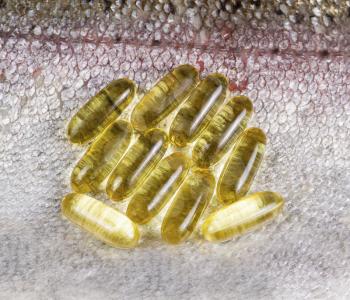 Several golden fish oil capsules place on top of fresh clean salmon skin