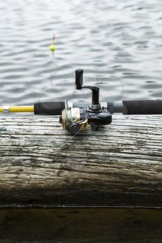 Fishing reel, rod on log with water and bobber in background