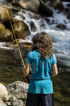 Young girl fishing in rapids of stream for trout during summer day