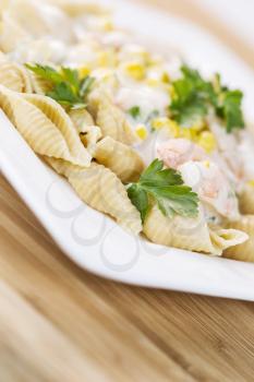 Vertical photo of alfredo pasta made of whole wheat shells, shrimp and parsley on white dish with natural bamboo wood underneath