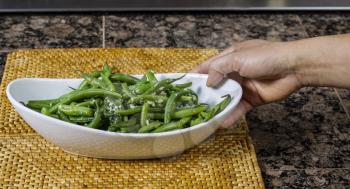 Fresh whole green beans in white bowl with hand placing them on mat