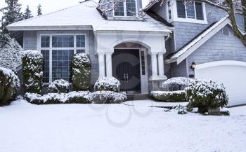 Horizontal photo of suburban home with snow on lawn, plants, trees and roof