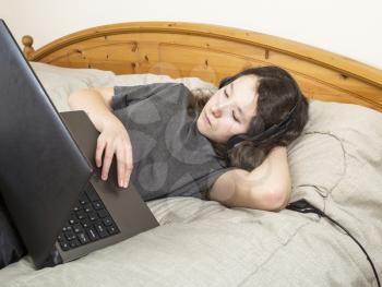 Young girl resting in bed while browsing the internet on her laptop computer