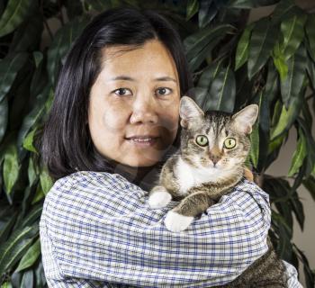 Mature Asian Women holding family cat with plant in background