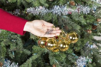 Female hand gathering golden ornaments to be put into storage with Christmas tree in background
