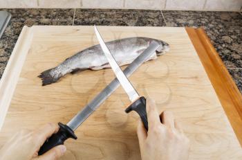 Female hand sharpening fillet knife with single fish on cutting board