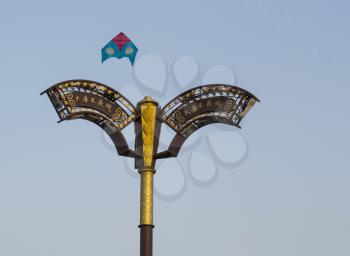 Chinese lamp post with kite flying above in blue sky and birds in background