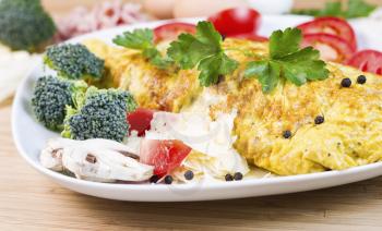 Horizontal photo of large egg omelet with mushroom, cheese, broccoli, tomato slices, pepper and parsley in white plate