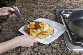 Horizontal photo with main focus on pancake being placed into white plate with large spatula