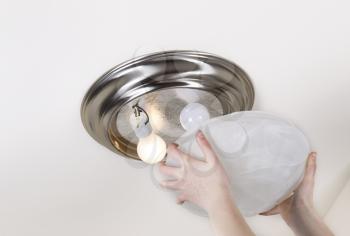 Horizontal photo hands taking of glass lid of ceiling lights- incandescent type- with one bulb burnt out and one working
